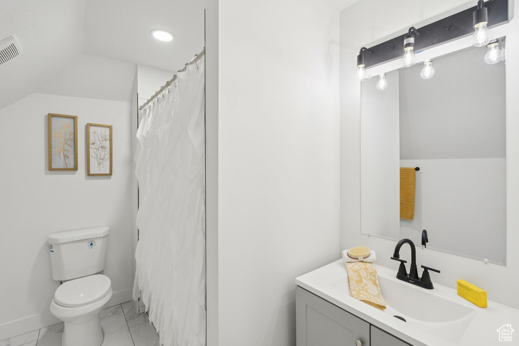 Full bathroom with vanity, marble look tiles, toilet, and vaulted ceiling