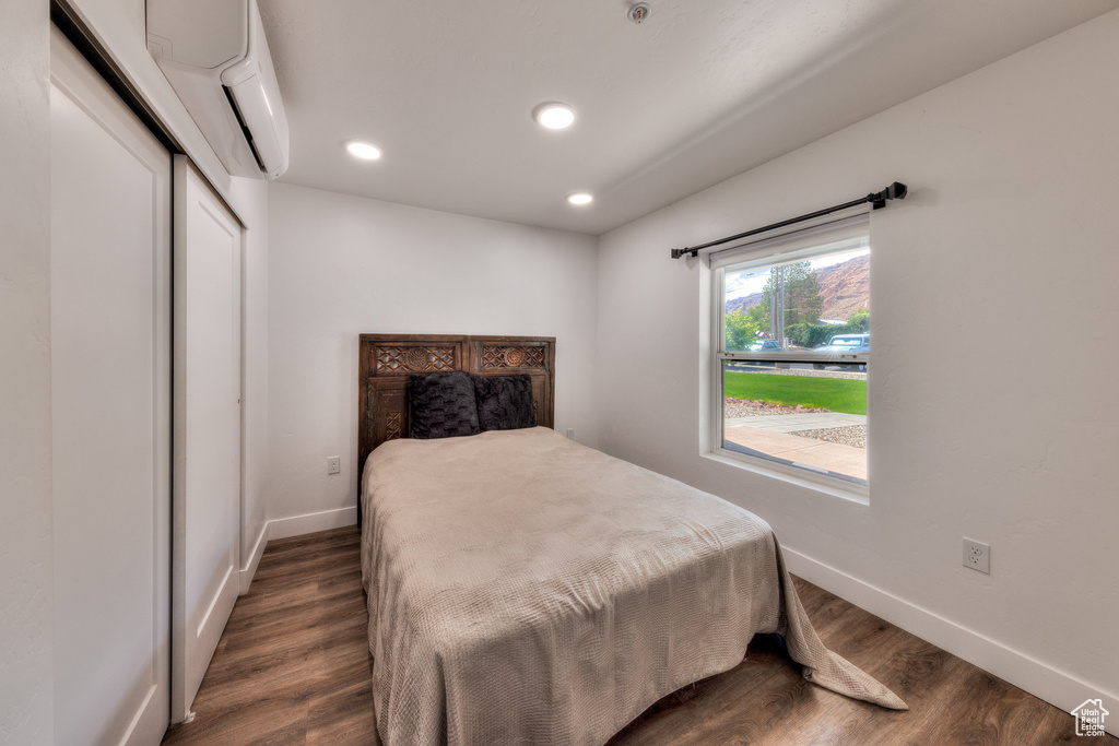 Bedroom with dark wood-style flooring, recessed lighting, a wall mounted air conditioner, and a closet