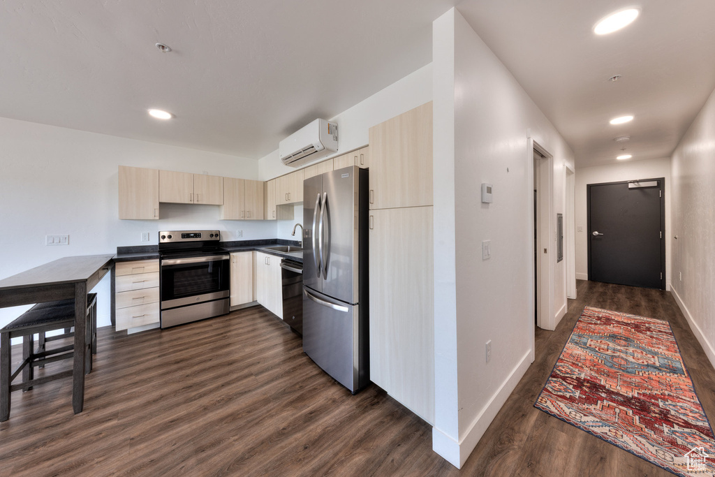 Kitchen with appliances with stainless steel finishes, a wall mounted air conditioner, dark countertops, dark wood-style flooring, and light brown cabinets