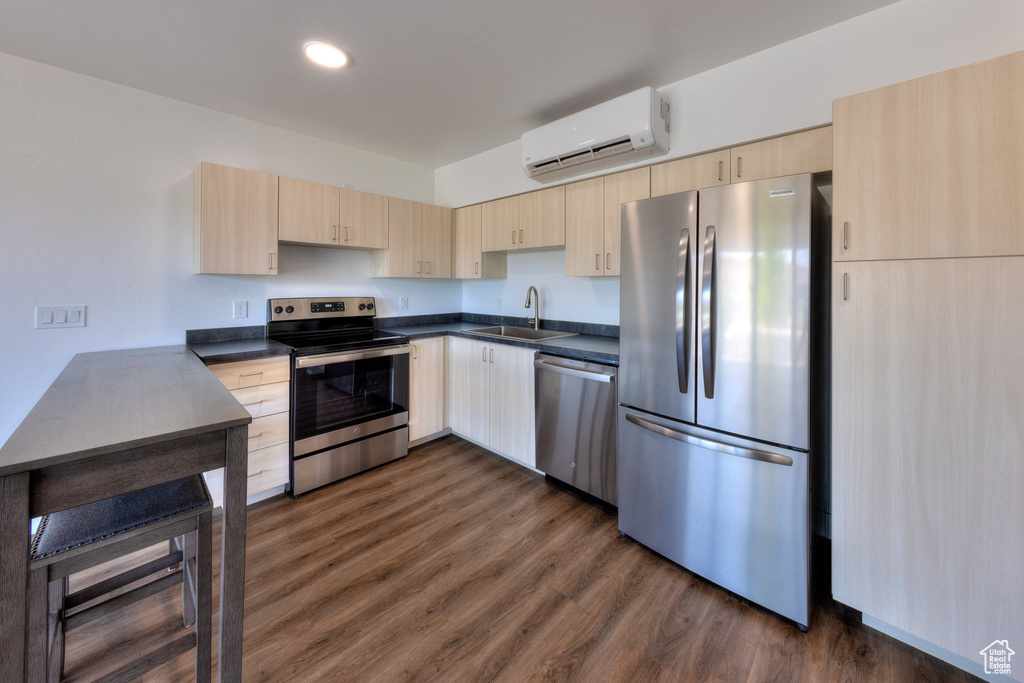 Kitchen with stainless steel appliances, light brown cabinetry, a wall unit AC, dark countertops, and recessed lighting