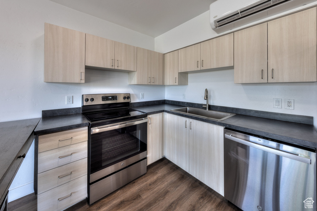 Kitchen featuring appliances with stainless steel finishes, light brown cabinetry, a wall unit AC, and dark countertops