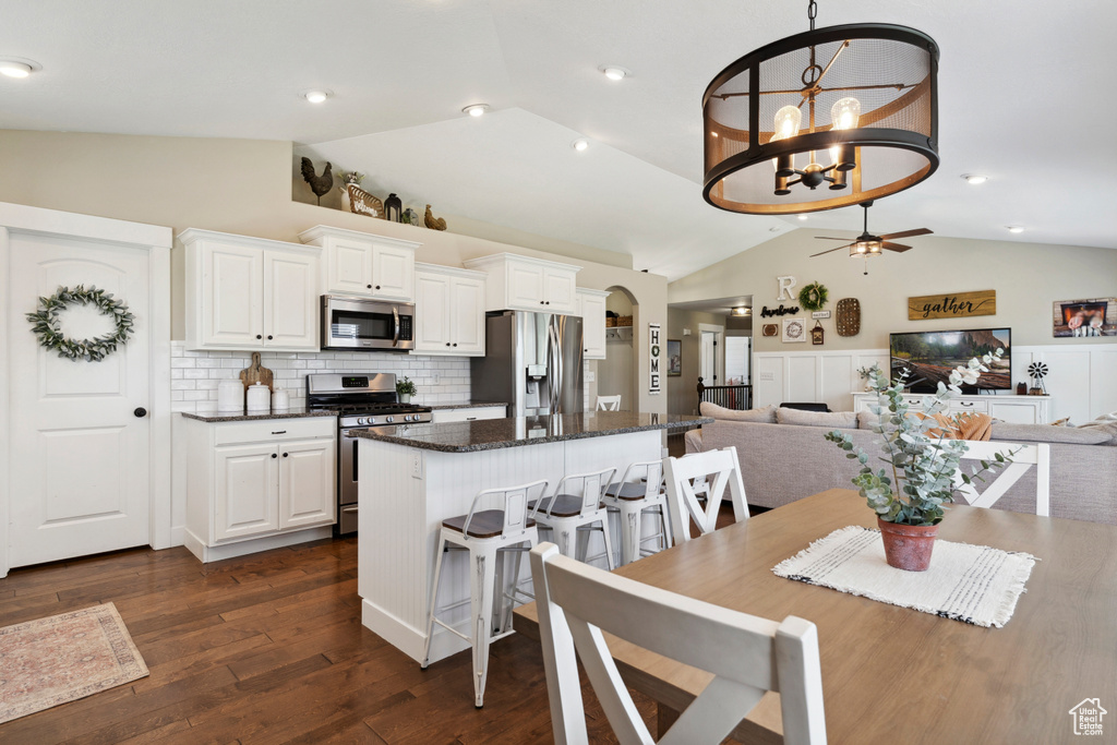 Dining room featuring vaulted ceiling, ceiling fan, dark wood-type flooring, a chandelier, and arched walkways