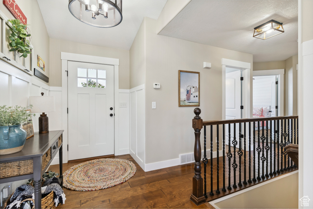 Entryway with wood-type flooring, a chandelier, and wainscoting