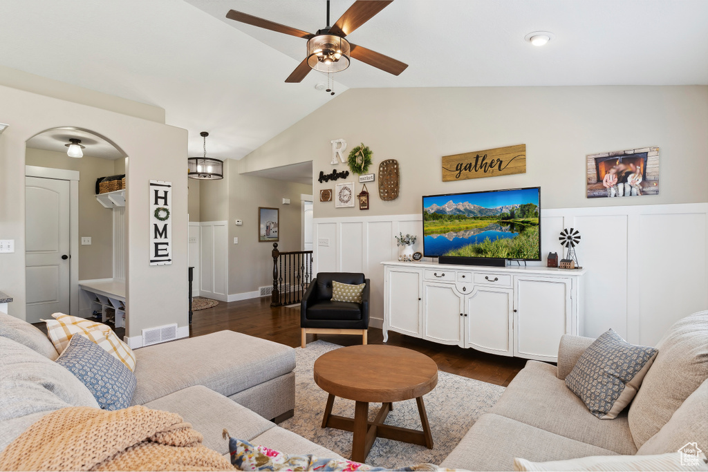 Living area with ceiling fan, dark wood-type flooring, wainscoting, vaulted ceiling, and a decorative wall