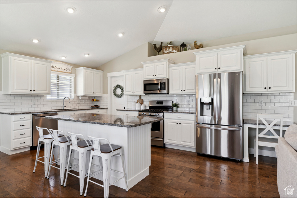 Kitchen featuring appliances with stainless steel finishes, a center island, a breakfast bar, decorative backsplash, and lofted ceiling