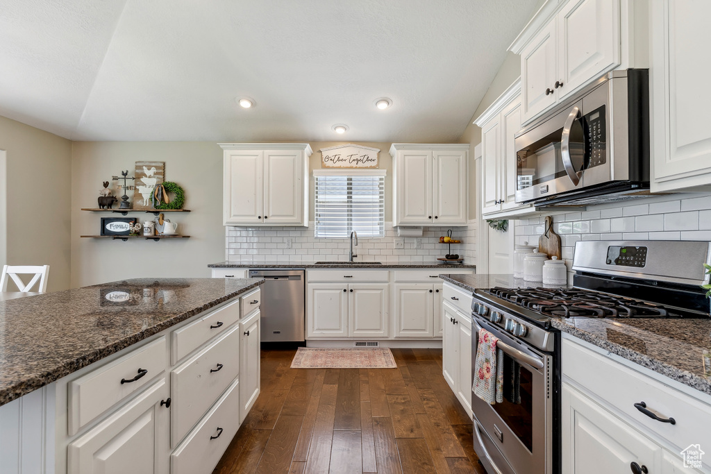 Kitchen with appliances with stainless steel finishes, dark wood finished floors, white cabinetry, tasteful backsplash, and dark stone counters