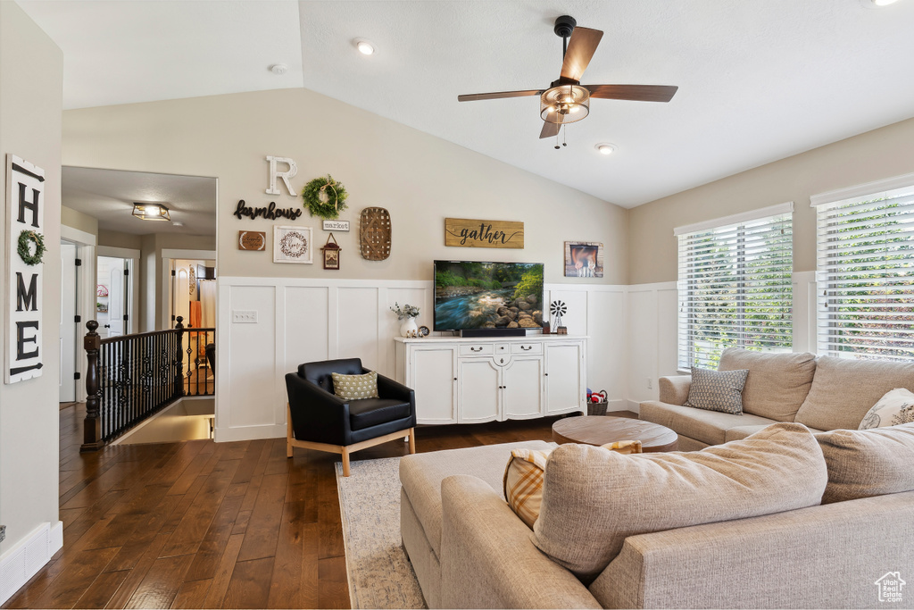 Living area with vaulted ceiling, a wainscoted wall, dark wood finished floors, ceiling fan, and a decorative wall