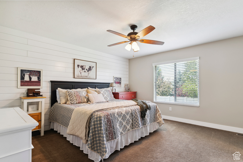 Bedroom featuring dark carpet, ceiling fan, and wooden walls