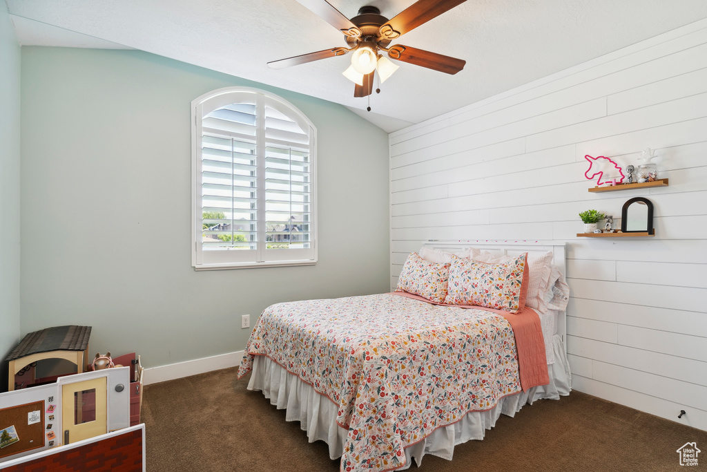Bedroom featuring dark colored carpet, wood walls, and a ceiling fan