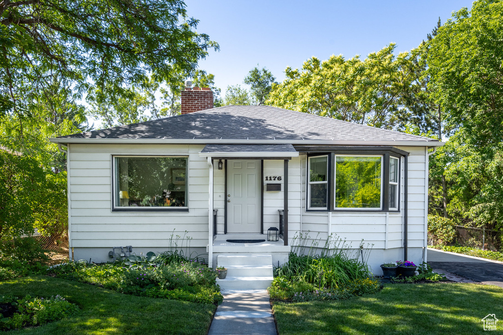 Bungalow featuring a chimney, a front lawn, and a shingled roof