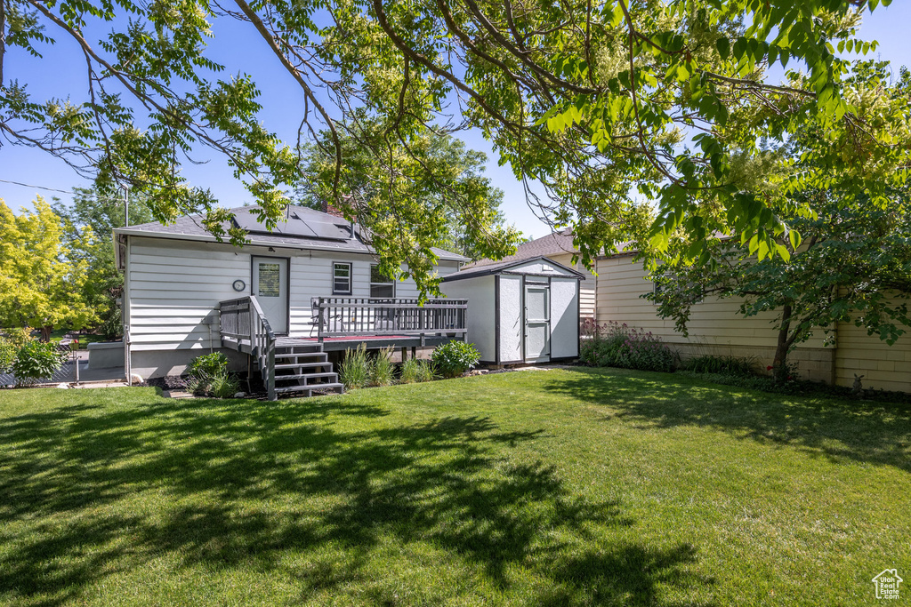 Rear view of property with a storage unit, a wooden deck, and a lawn