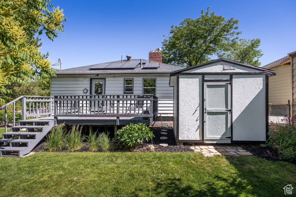 Rear view of property with a storage shed, a yard, a chimney, solar panels, and a deck