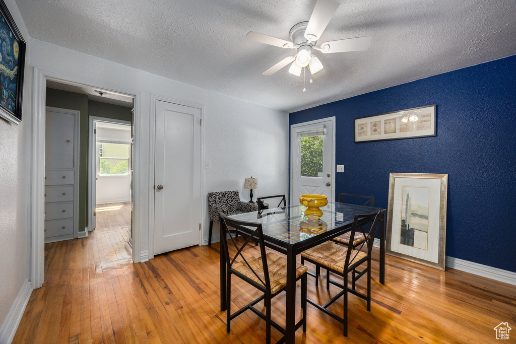 Dining room with hardwood / wood-style flooring, healthy amount of natural light, a ceiling fan, a textured ceiling, and a textured wall