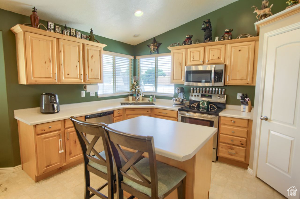 Kitchen with stainless steel appliances, light brown cabinetry, lofted ceiling, light countertops, and recessed lighting