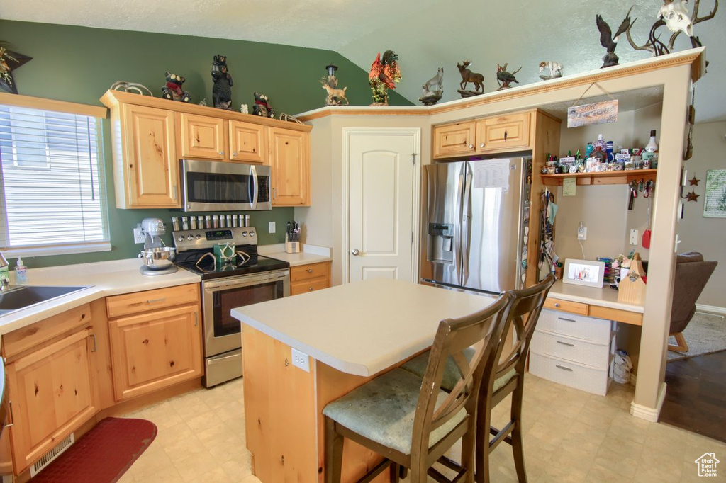 Kitchen featuring stainless steel appliances, light brown cabinets, light countertops, vaulted ceiling, and light floors
