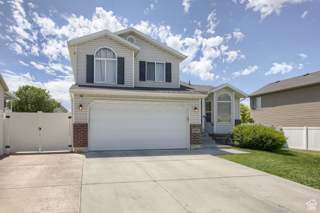 Traditional home featuring brick siding, a gate, driveway, an attached garage, and entry steps