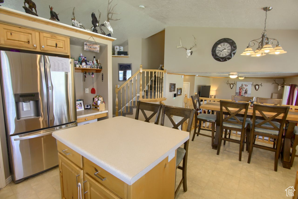 Kitchen with stainless steel fridge, vaulted ceiling, light countertops, light flooring, and a kitchen island