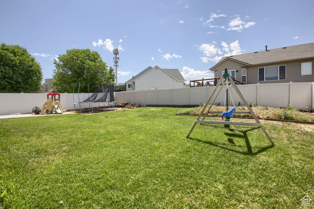 Fenced backyard featuring a trampoline and a playground