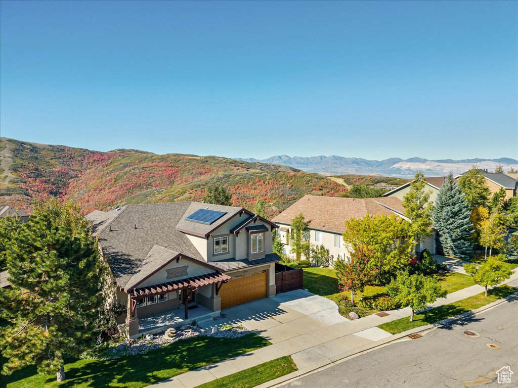 View of front facade with driveway, an attached garage, roof mounted solar panels, and a mountain view