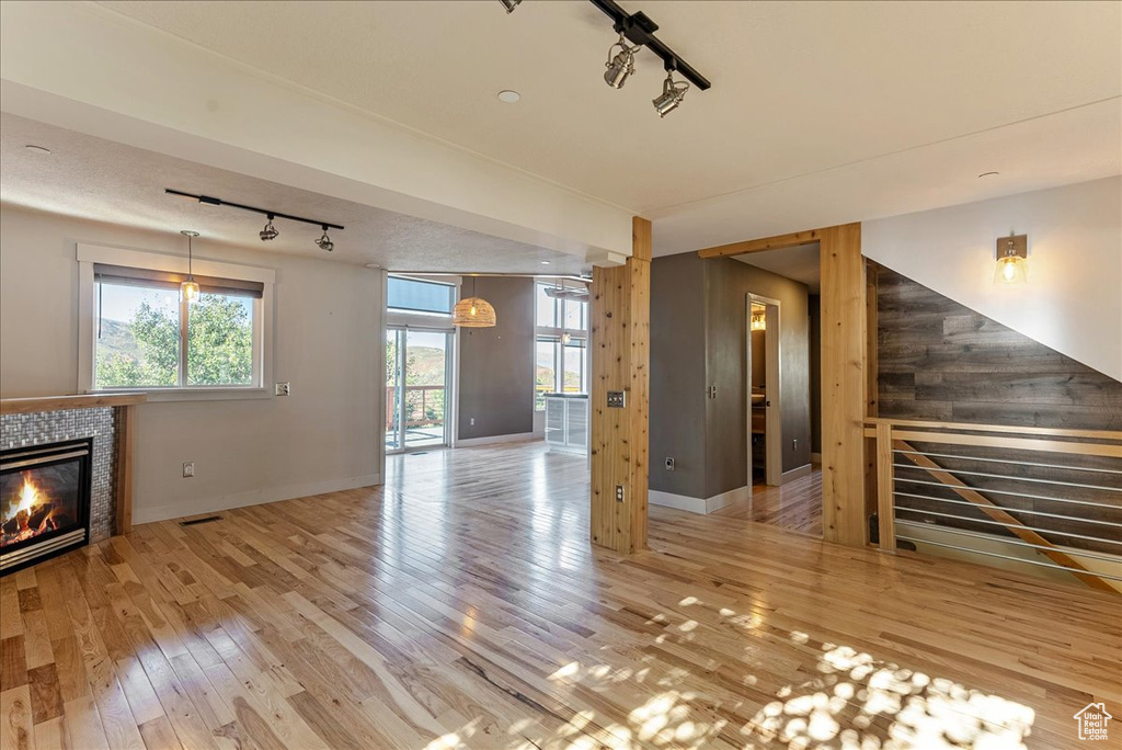 Unfurnished living room with rail lighting, a fireplace, wood finished floors, and baseboards