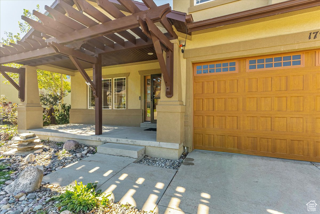 Doorway to property with stucco siding, a porch, a garage, and a pergola