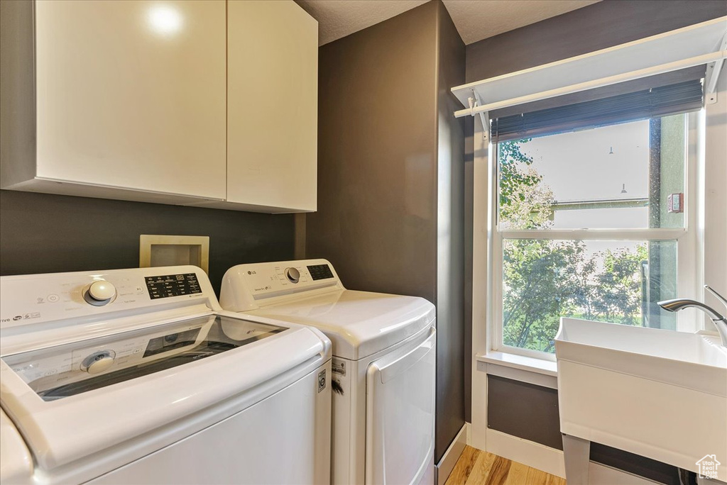 Laundry area featuring cabinet space, separate washer and dryer, light wood-style floors, and baseboards