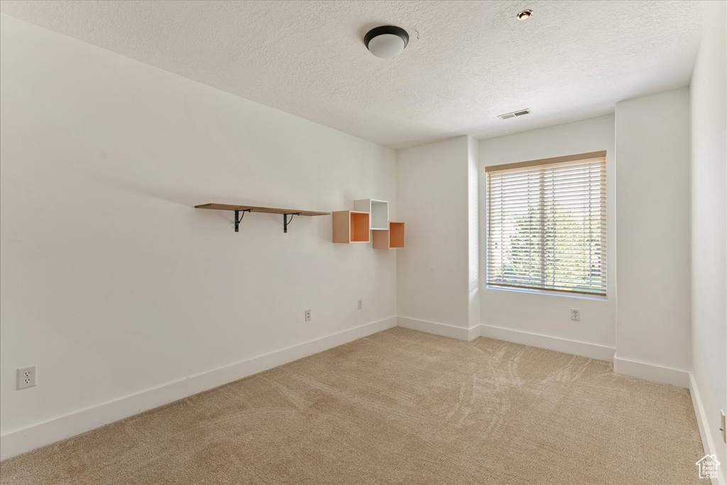 Spare room with light carpet, a textured ceiling, and baseboards