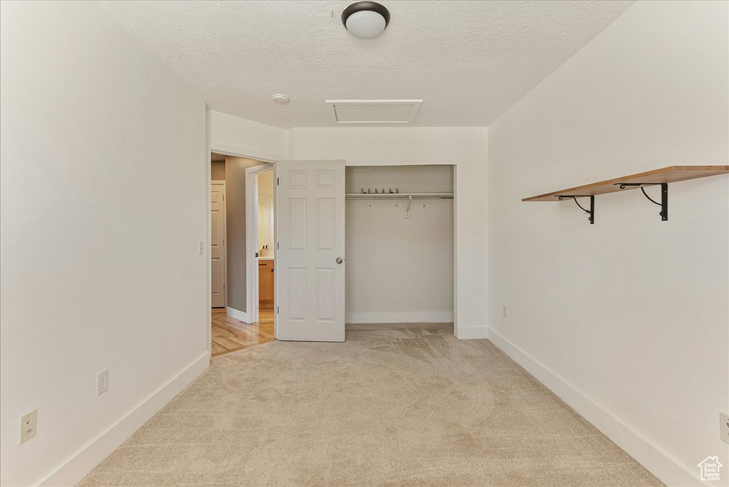 Unfurnished bedroom with light carpet, a textured ceiling, attic access, baseboards, and a closet