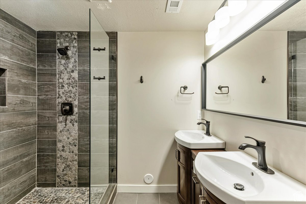 Full bathroom featuring tile patterned floors, a tile shower, two vanities, and baseboards