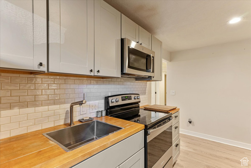 Kitchen featuring appliances with stainless steel finishes, a sink, baseboards, light wood-style flooring, and tasteful backsplash