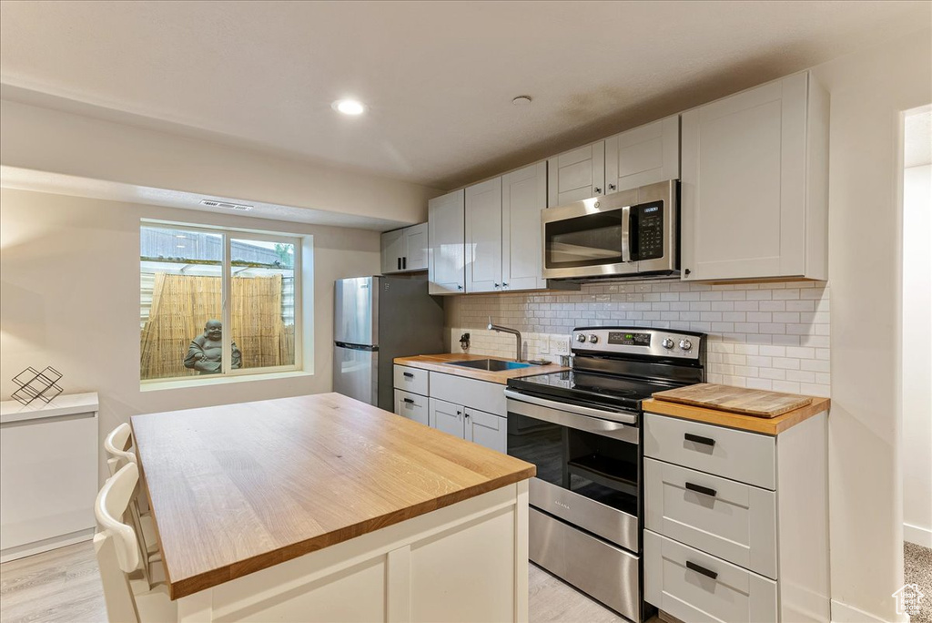 Kitchen with appliances with stainless steel finishes, wooden counters, a sink, backsplash, and recessed lighting