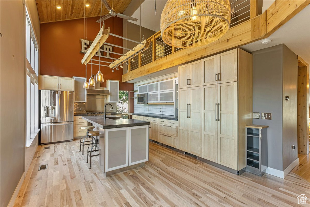 Kitchen with stainless steel refrigerator with ice dispenser, high vaulted ceiling, dark countertops, light wood-style floors, and backsplash