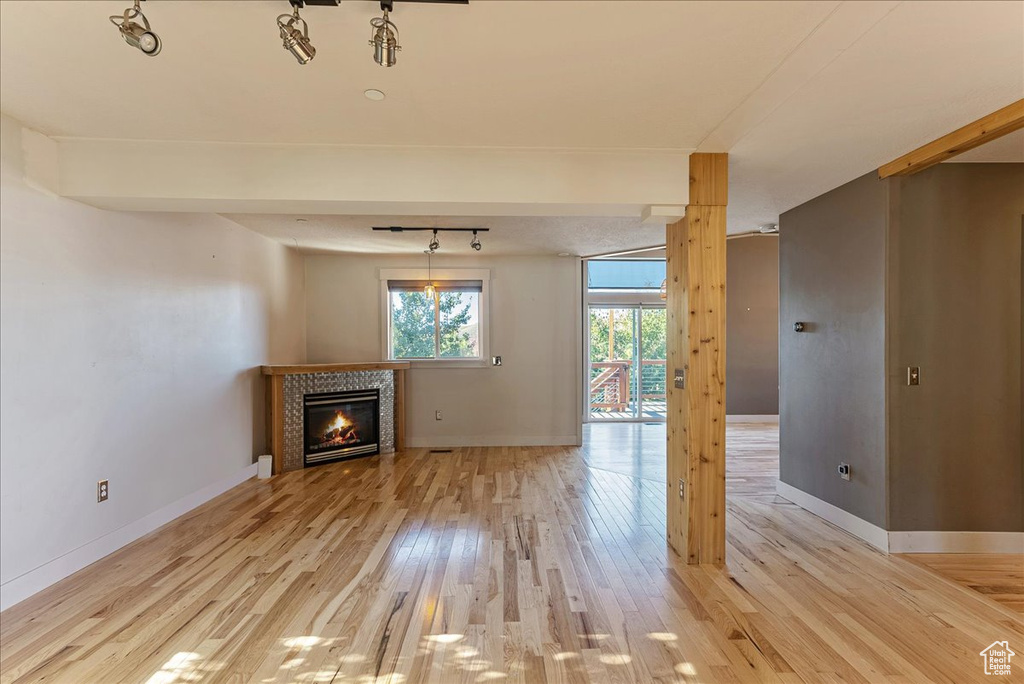 Unfurnished living room featuring light wood-style floors, a fireplace, baseboards, and rail lighting