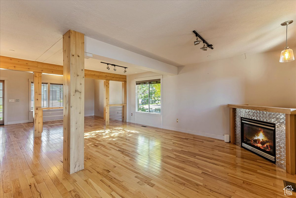 Unfurnished living room featuring track lighting, light wood finished floors, a fireplace, baseboards, and a textured ceiling