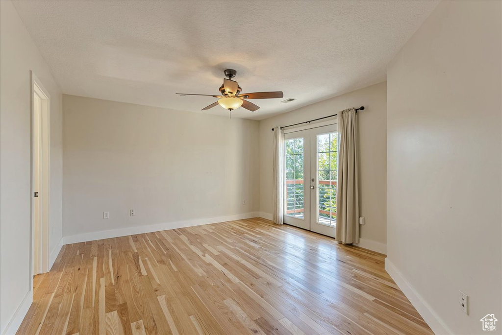 Spare room with french doors, light wood finished floors, ceiling fan, baseboards, and a textured ceiling