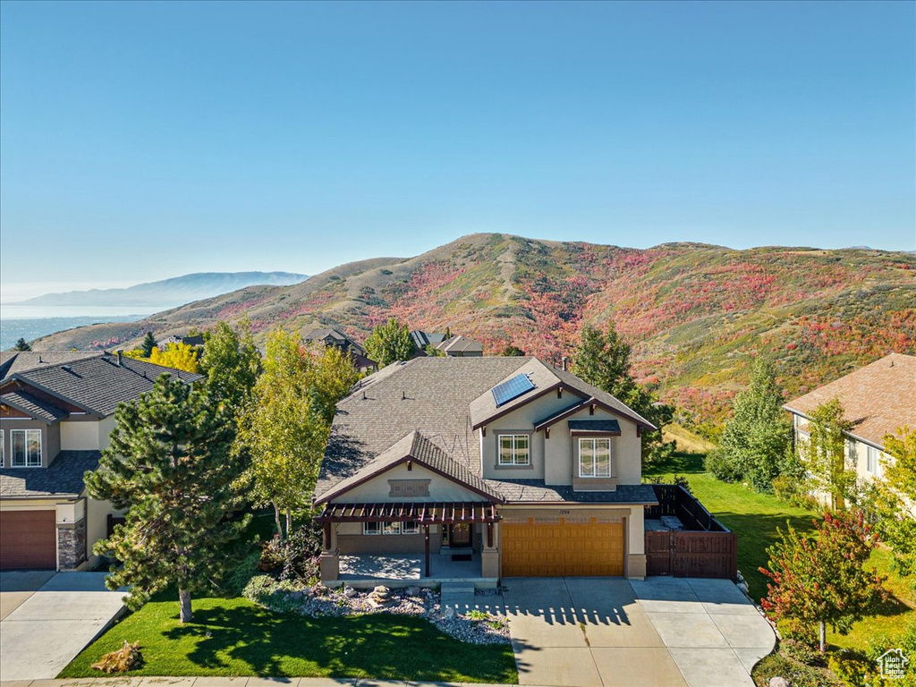 View of front of home with driveway, a garage, solar panels, stucco siding, and a mountain view