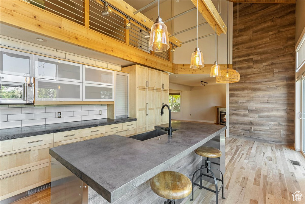 Kitchen featuring a sink, a high ceiling, wood walls, dark countertops, and light brown cabinetry