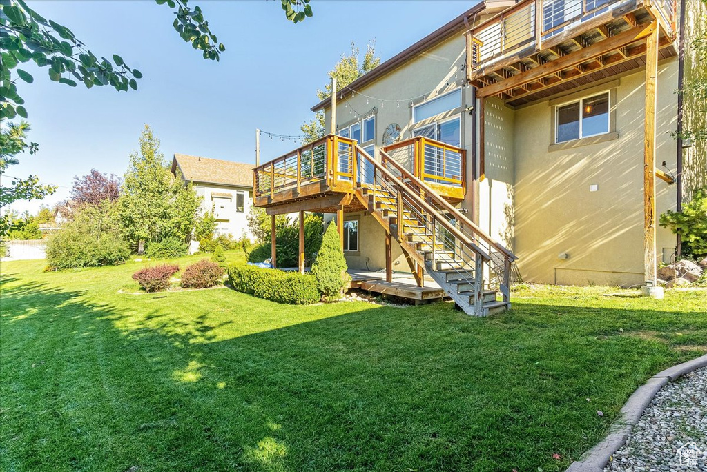 Back of house with a wooden deck, stairway, a lawn, and stucco siding