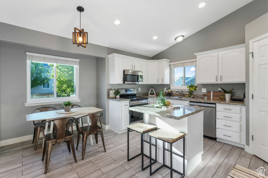 Kitchen featuring appliances with stainless steel finishes, white cabinetry, vaulted ceiling, light stone countertops, and recessed lighting