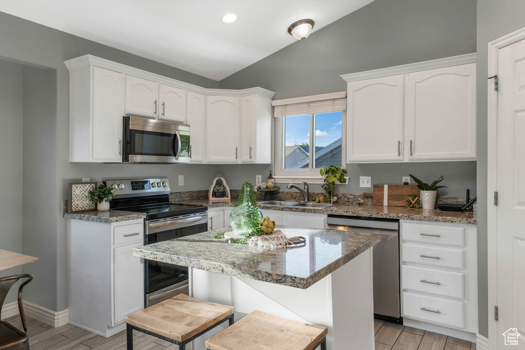 Kitchen with appliances with stainless steel finishes, vaulted ceiling, white cabinets, wood tiled floors, and stone countertops