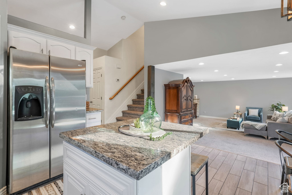 Kitchen with stainless steel refrigerator with ice dispenser, white cabinets, light stone counters, a center island, and lofted ceiling