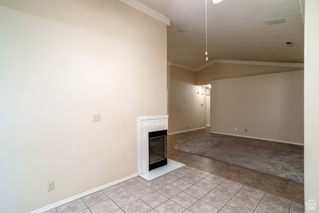 Unfurnished living room featuring light tile patterned floors, lofted ceiling, baseboards, a high end fireplace, and light carpet