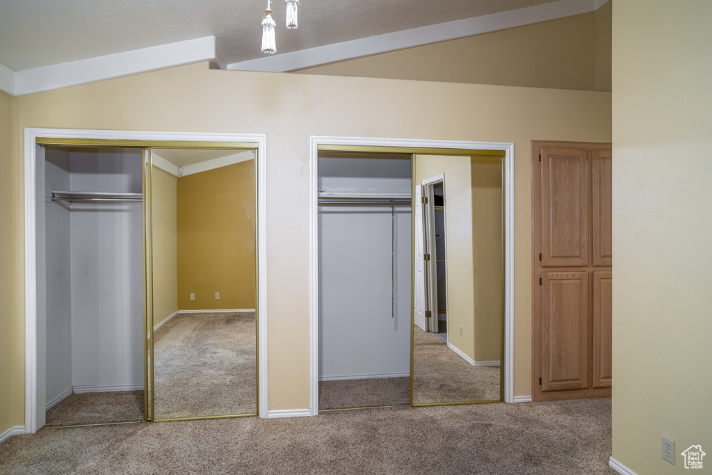 Unfurnished bedroom with carpet floors, two closets, lofted ceiling, and baseboards