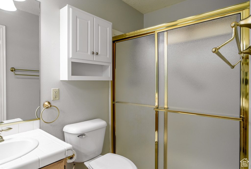 Bathroom with vanity, a shower with shower door, and toilet