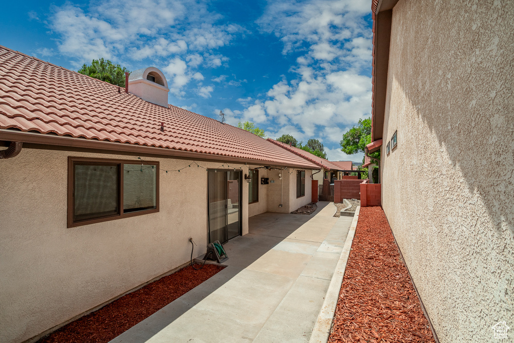 View of side of home featuring stucco siding, a tiled roof, a patio, and a chimney