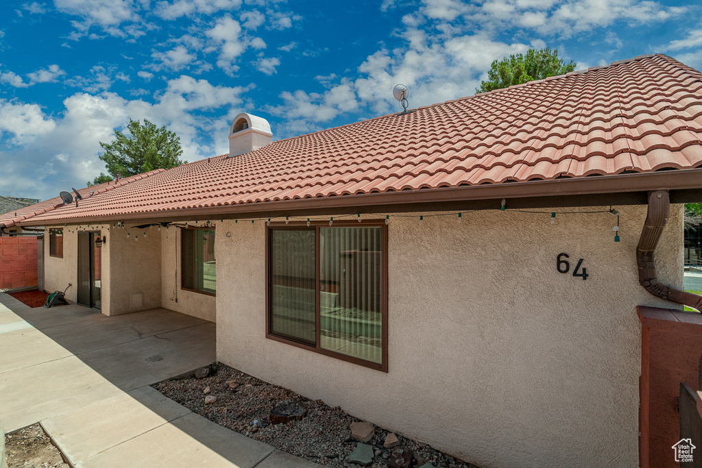 Back of property with stucco siding, a tile roof, a patio area, and a chimney