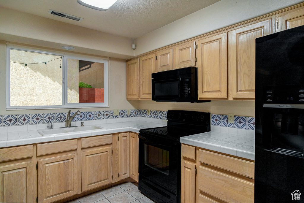 Kitchen featuring black appliances, a sink, tasteful backsplash, light tile patterned floors, and light brown cabinetry