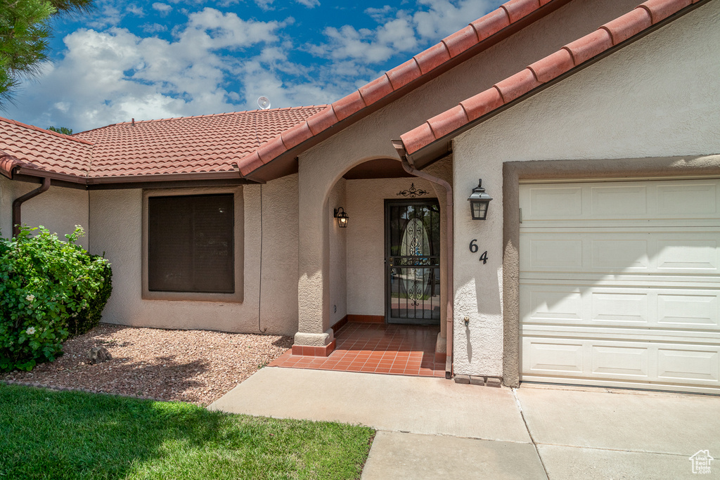 Property entrance with stucco siding, a tiled roof, and an attached garage