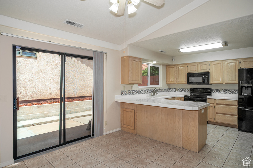Kitchen with black appliances, light brown cabinetry, a sink, a peninsula, and lofted ceiling