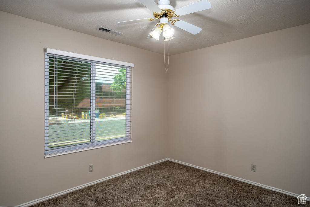 Empty room featuring dark colored carpet, ceiling fan, a textured ceiling, and baseboards
